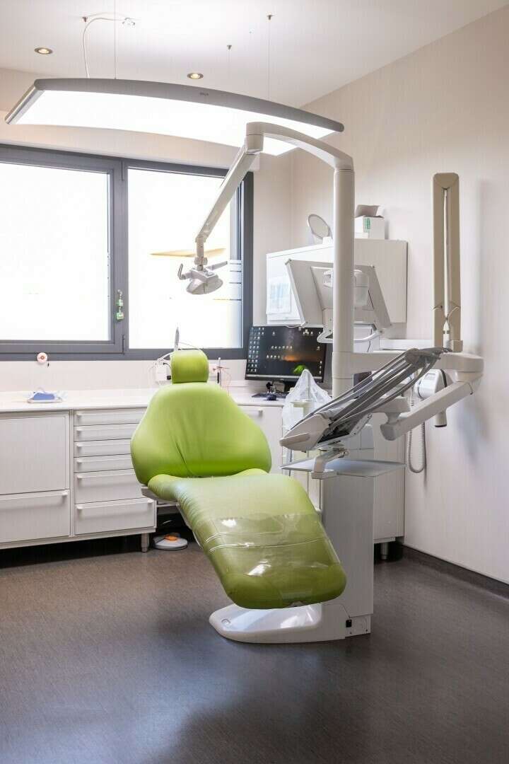 Une salle de soins du cabinet, fauteuil et scialytique près de la fenêtre